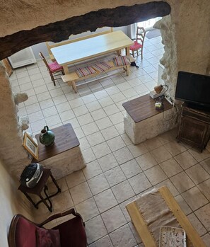 Une pièce rustique avec un sol carrelé, une table en bois entourée de chaises, un téléviseur posé sur un meuble en bois et une carte géographique sur une autre table en bois.