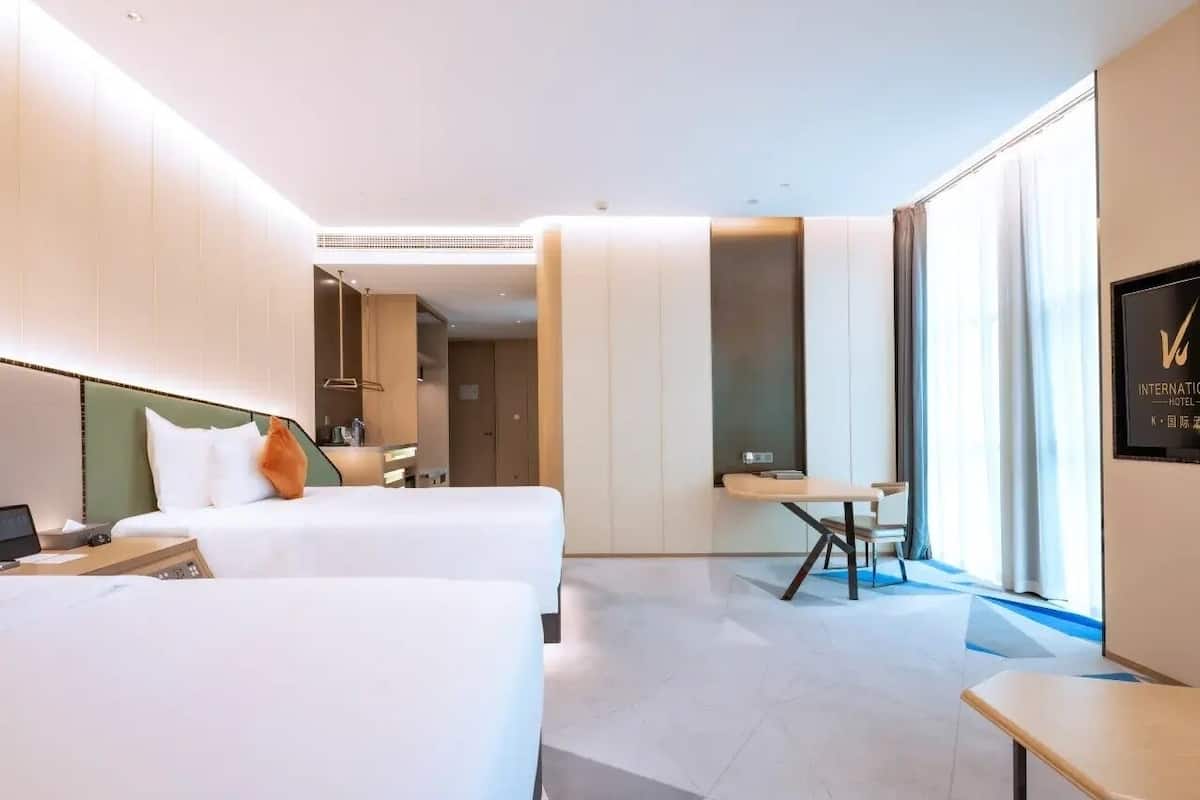 A modern hotel room with two beds, a desk, and a chair.