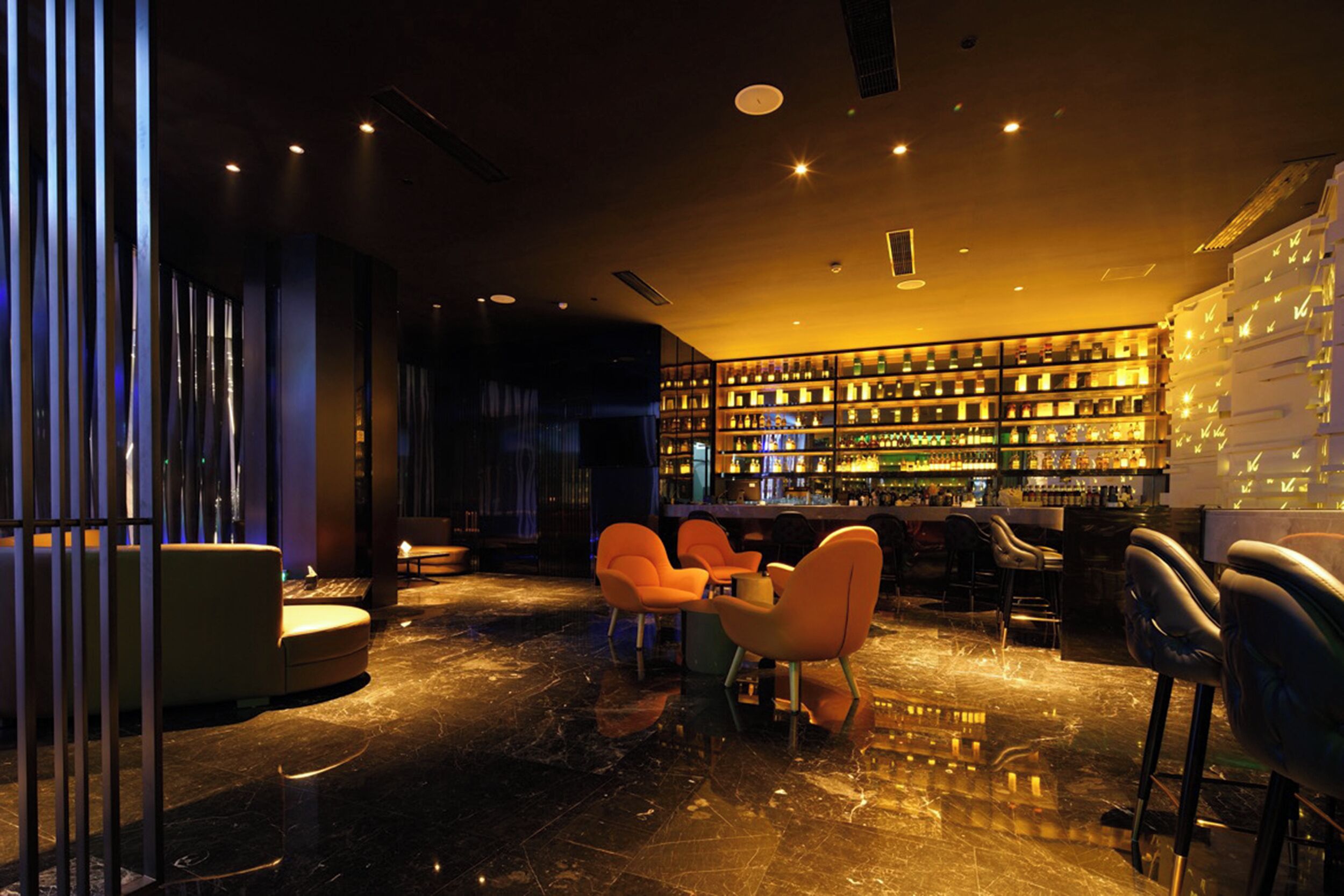Uma área de bar moderna com assentos e uma prateleira de bebidas bem abastecida.