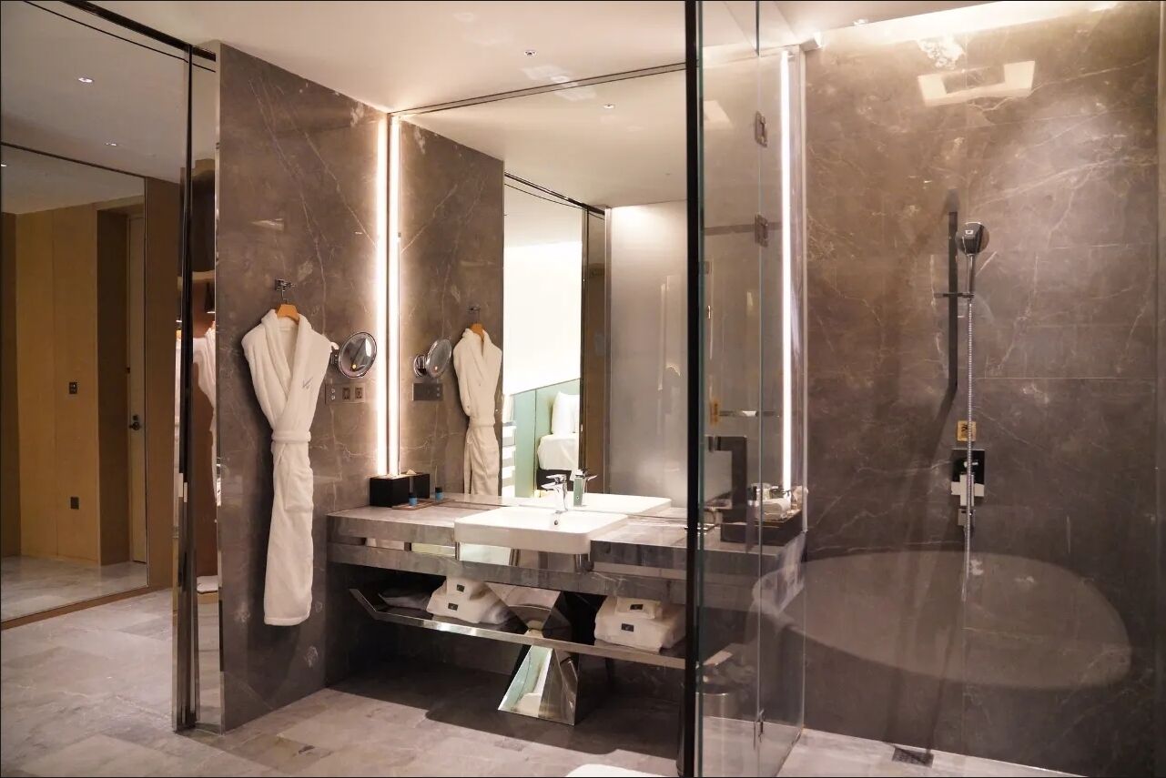 A modern bathroom with a glass-enclosed shower, a large mirror, and a vanity with a sink and towel rack.