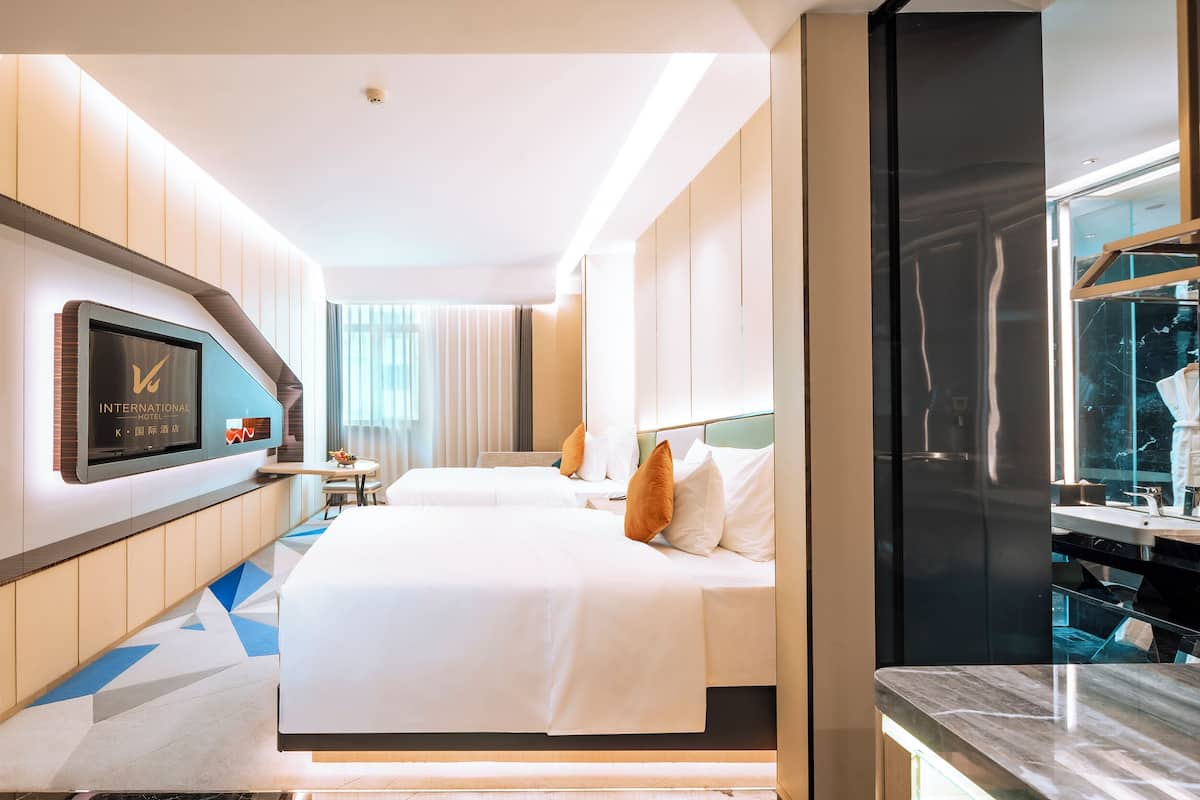 A hotel room with two beds, a TV, a minibar, and a large window.