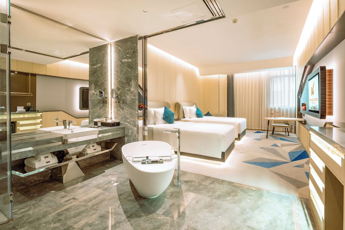 A modern hotel room with a marble bathroom, a large bed, a TV, and a desk.