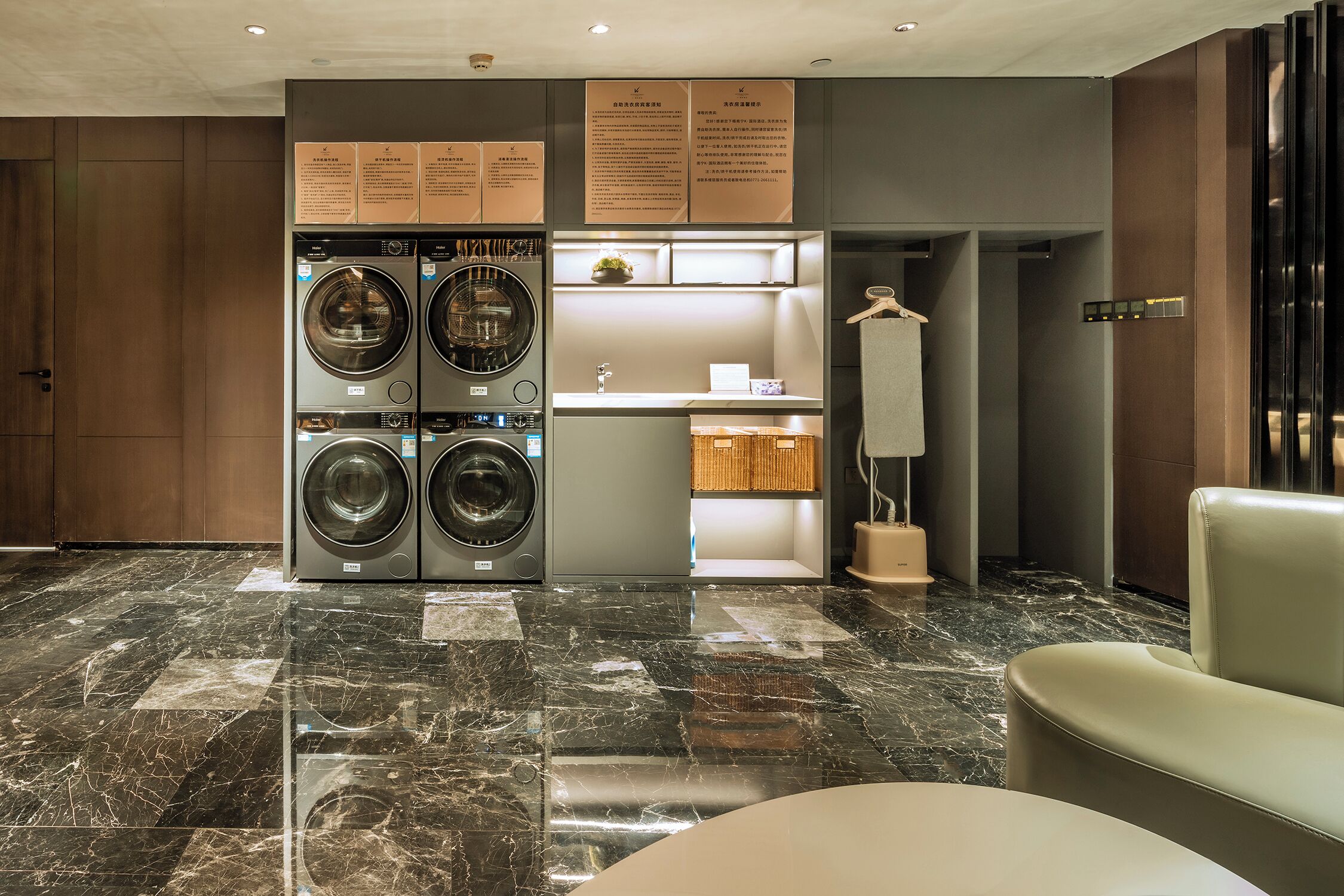 A modern hotel room with a marble floor, a built-in washer and dryer, a small kitchenette, and a seating area.