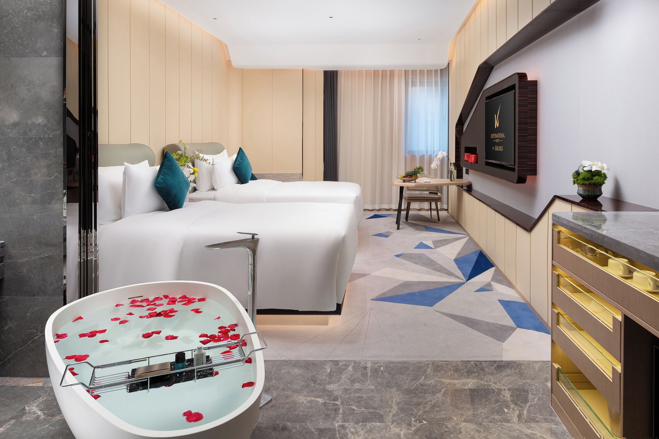 Una habitación de hotel con una cama grande, un área de estar separada, una bañera con pétalos de rosa y un televisor montado en la pared.