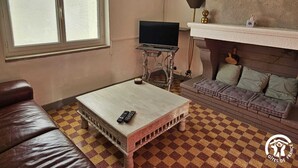 A room with a checkered floor, a television on a stand, a sofa, and a fireplace. - l'Oustal des Margaridous (LABRUGUIERE)