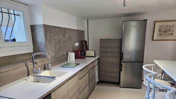 A modern kitchen with a stainless steel refrigerator, a built-in dishwasher, and a bar area with stools. - l'Oustal des Margaridous (LABRUGUIERE)