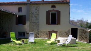 A stone building with a tiled roof, a small balcony, and a grassy area with several lounge chairs. - l'Oustal des Margaridous (LABRUGUIERE)