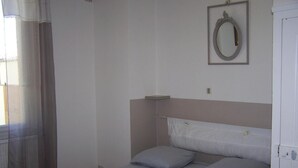 A bedroom with a bed, pillows, a nightstand, a mirror, and a window with curtains. - l'Oustal des Margaridous (LABRUGUIERE)