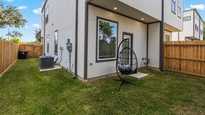 A modern two-story house with a covered patio, a wooden fence, and a large air conditioning unit. - Modern 3BR Home w/Private Yard + Garage (Houston)