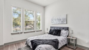 A bedroom with a bed, a nightstand, a lamp, and a painting on the wall. - Modern 3BR Home w/Private Yard + Garage (Houston)
