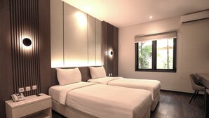 A modern hotel room with two beds, a bedside table with a phone, and a window with a view of palm trees.