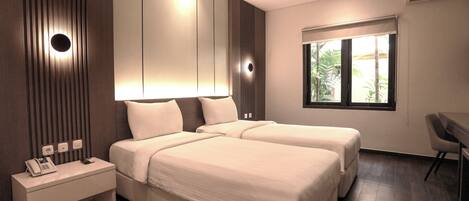 Habitación de hotel moderna con dos camas, una mesita de noche con teléfono y ventana con vista a palmeras.