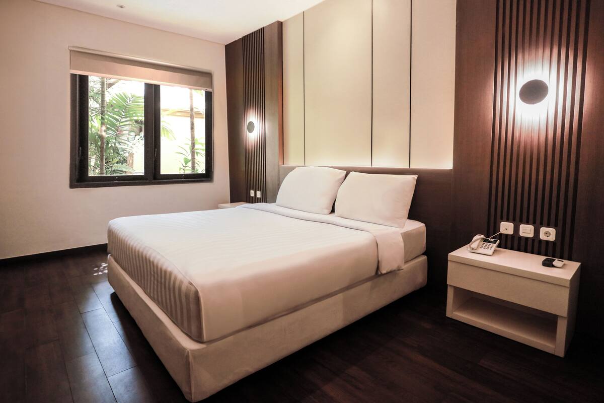 Une chambre moderne avec un grand lit, une table de chevet avec un téléphone et une fenêtre équipée de stores.