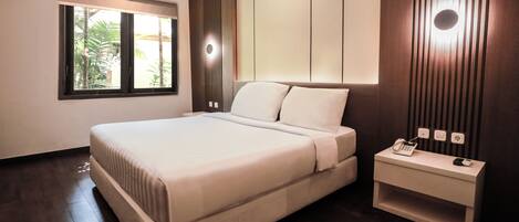 A modern bedroom with a large bed, a bedside table with a phone, and a window with blinds.
