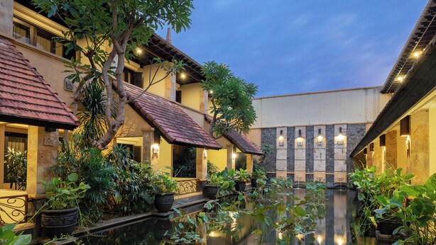 A serene courtyard with a reflective water feature, surrounded by lush greenery and traditional architecture.