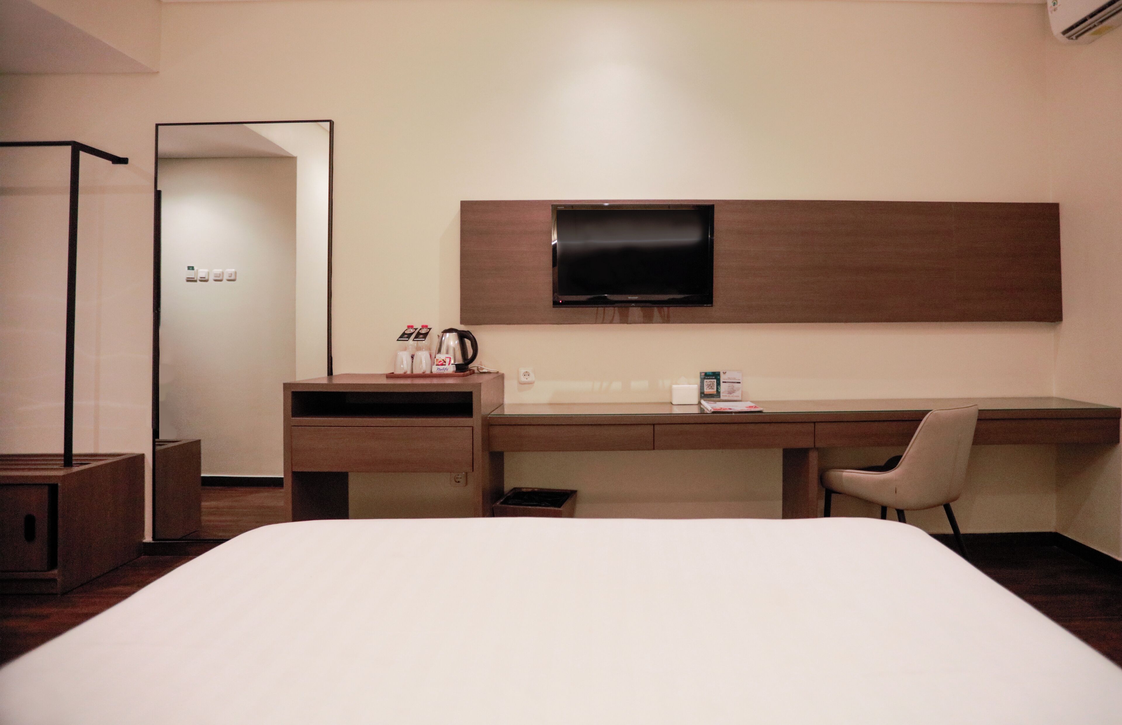 Hotelkamer met een bed, een bureau met stoel, een flatscreen televisie aan de muur, een kapstok en een tafeltje met waterkoker en kopjes.