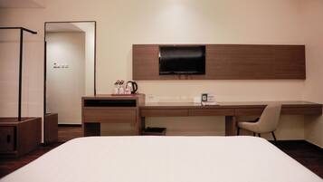 Hotelkamer met een bed, een bureau met stoel, een flatscreen televisie aan de muur, een kapstok en een tafeltje met waterkoker en kopjes.
