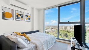 A modern hotel room with a large bed, a gray sofa, and a large window offering a city view. - Marvellous Views - Bright & Spacious CBD Escape (Melbourne)
