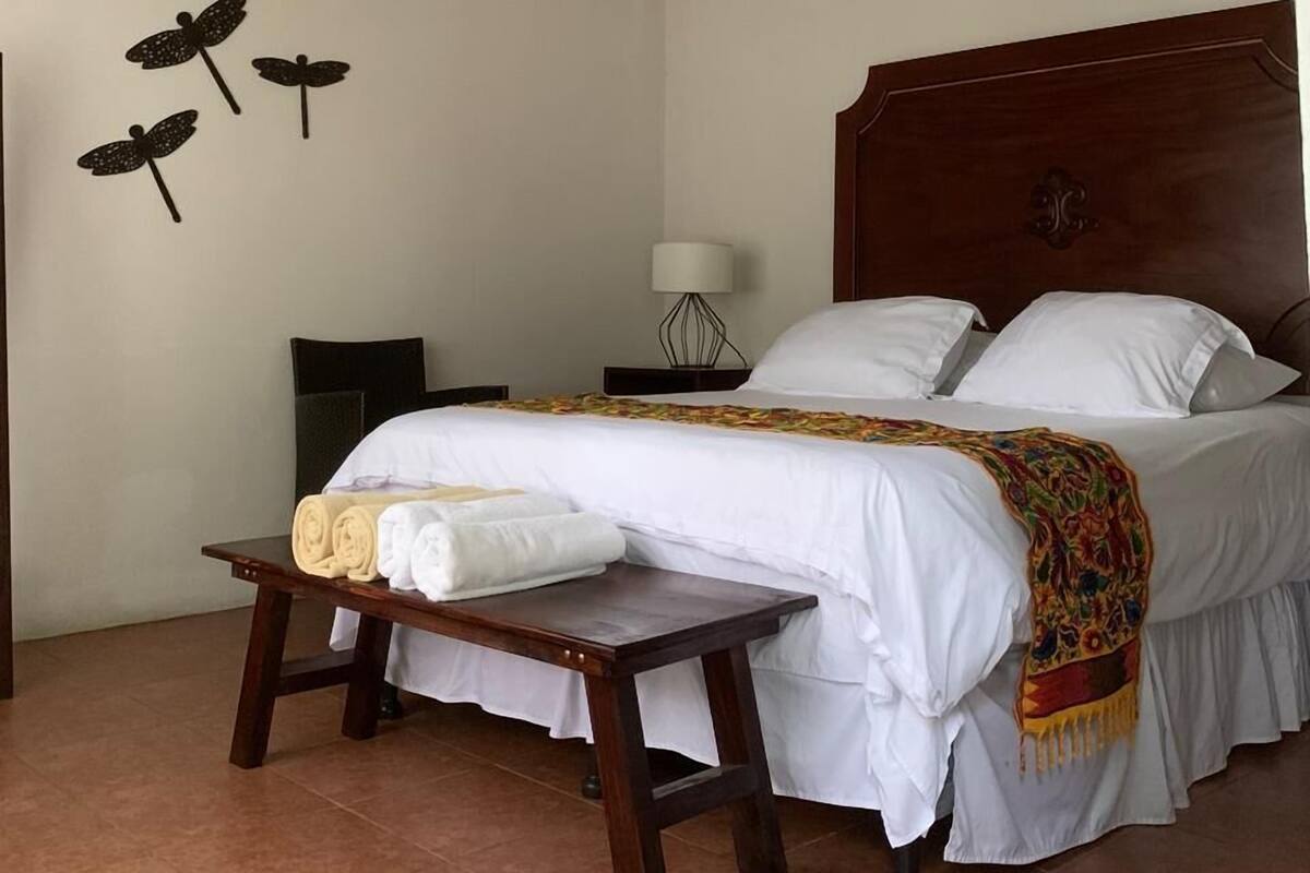 Une chambre à coucher comprenant un lit, une table de chevet, une table avec des serviettes, un ventilateur de plafond et des œuvres d’art murales.