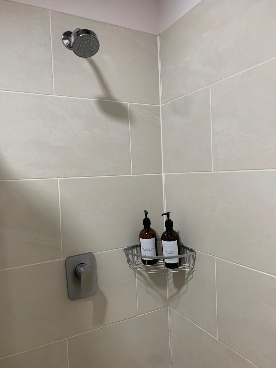 Un baño con ducha, un secador de manos y dos botellas de champú y acondicionador en un estante.
