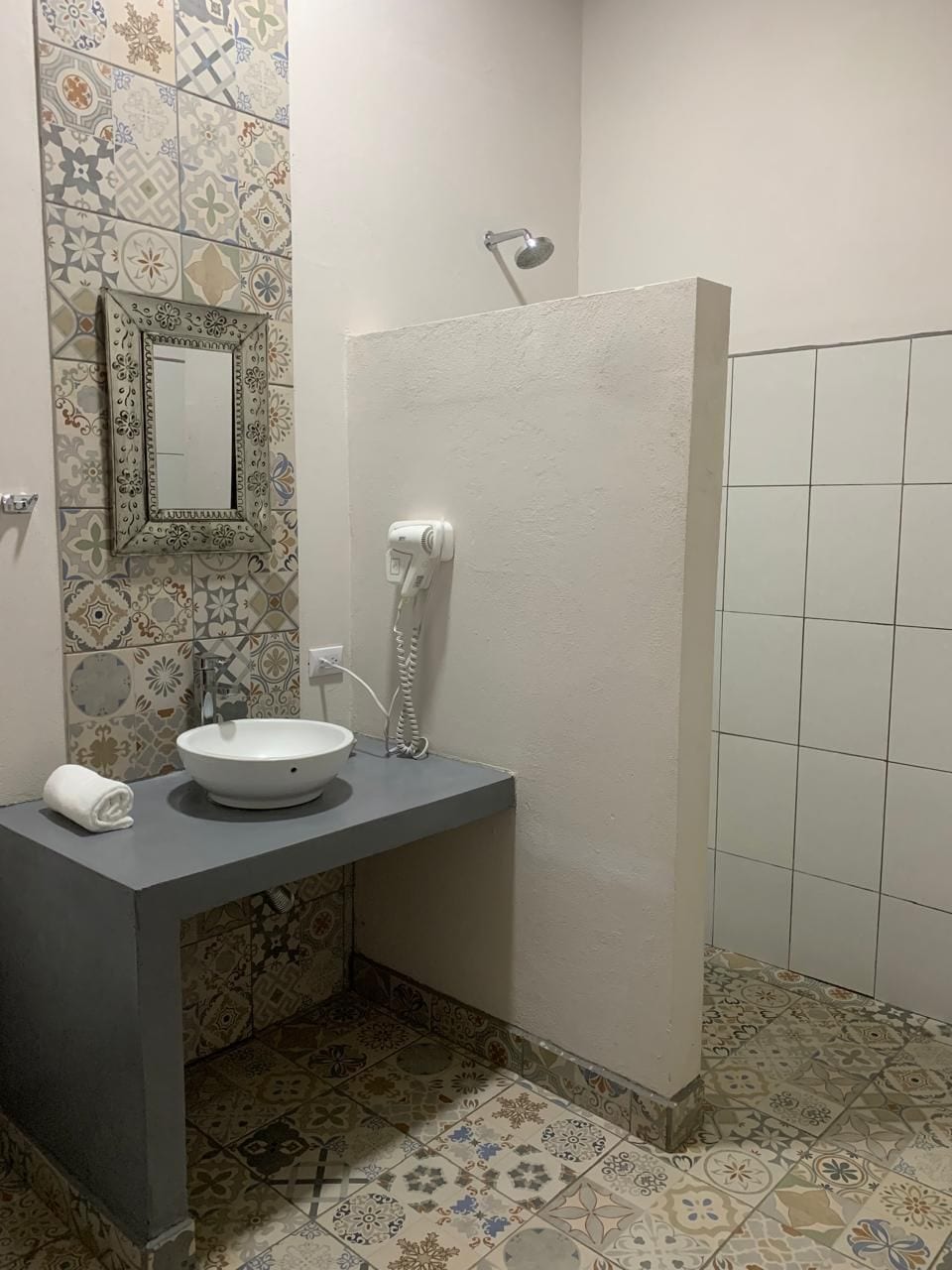 Une salle de bain avec un lavabo blanc, un miroir, un sèche-cheveux et des carreaux décoratifs sur les murs et le sol.