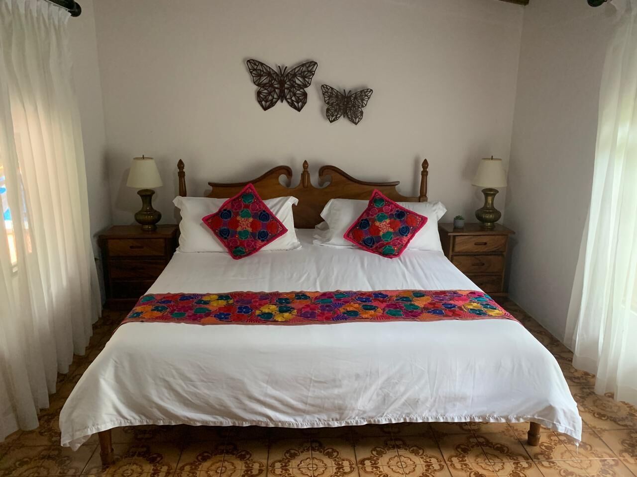 Ein Bett mit weißer Bettwäsche, zwei Zierkissen, einer farbenfrohen Decke und zwei Wanddekorationen mit Schmetterlingsmotiven.