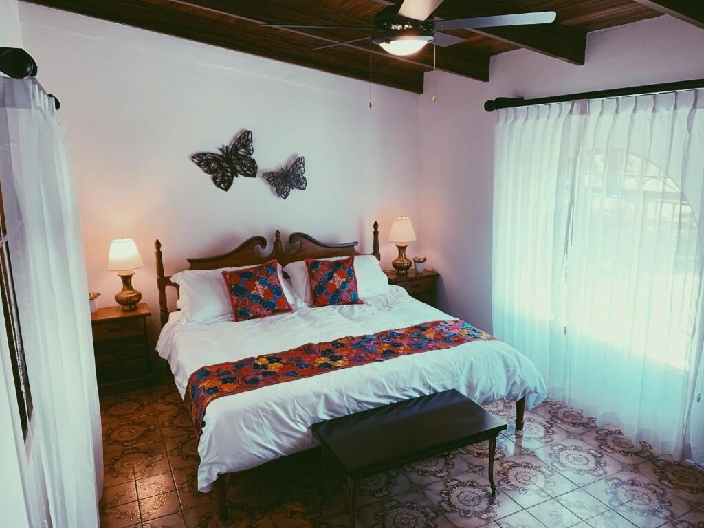 Une chambre avec un lit en bois, deux lampes de chevet, un ventilateur de plafond et une décoration murale représentant des papillons.