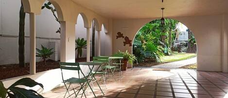 A covered patio area with tiled flooring, green folding chairs, potted plants, and a hanging lantern.