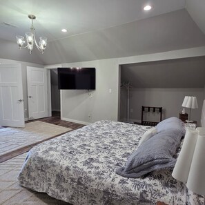 Ein Schlafzimmer mit einem großen Bett, einem flachbildfernseher an der Wand, einer Kristallleuchter und einem begehbaren Kleiderschrank.
