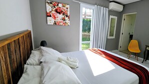 Een slaapkamer met een bed, bureau, stoel, spiegel en een raam met gordijnen.