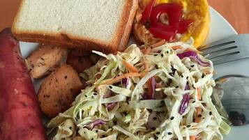 A plate with coleslaw, a slice of bread, a sausage, and a half of a red bell pepper. There is also a cup of coffee.