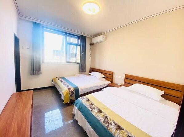 A hotel room with two single beds, a wooden desk, a window with curtains, and an air conditioning unit.