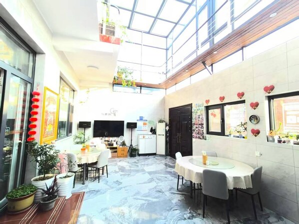 A spacious indoor area with a high ceiling, a dining table, chairs, and potted plants. - Gubeikou Great WallJuyouyuan Homestay (Miyun)