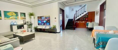 A modern living room with a flat-screen TV, a sofa, a coffee table, and a dining area with a table and chairs.