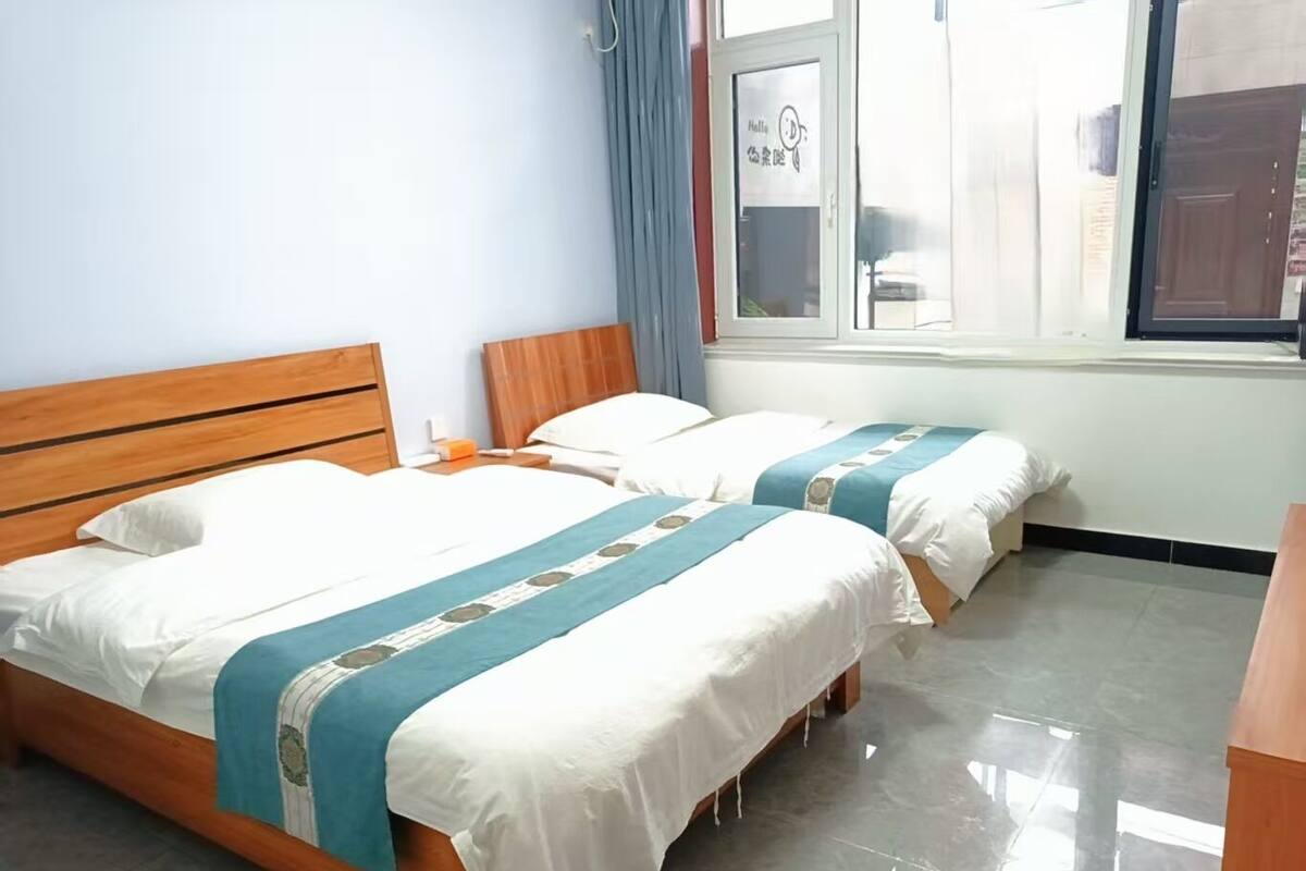 A hotel room with two beds, wooden headboards, and a window with curtains.
