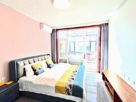 A bedroom with a bed, a nightstand, a wooden bench, and a large window with curtains.