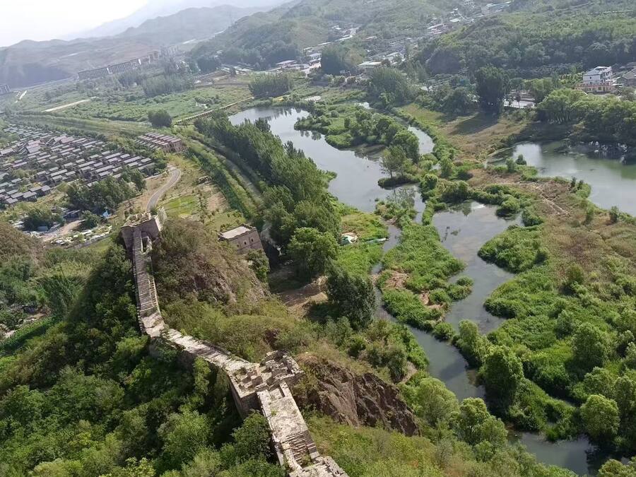 An aerial view of a historic site with ancient ruins, a river, and surrounding greenery.