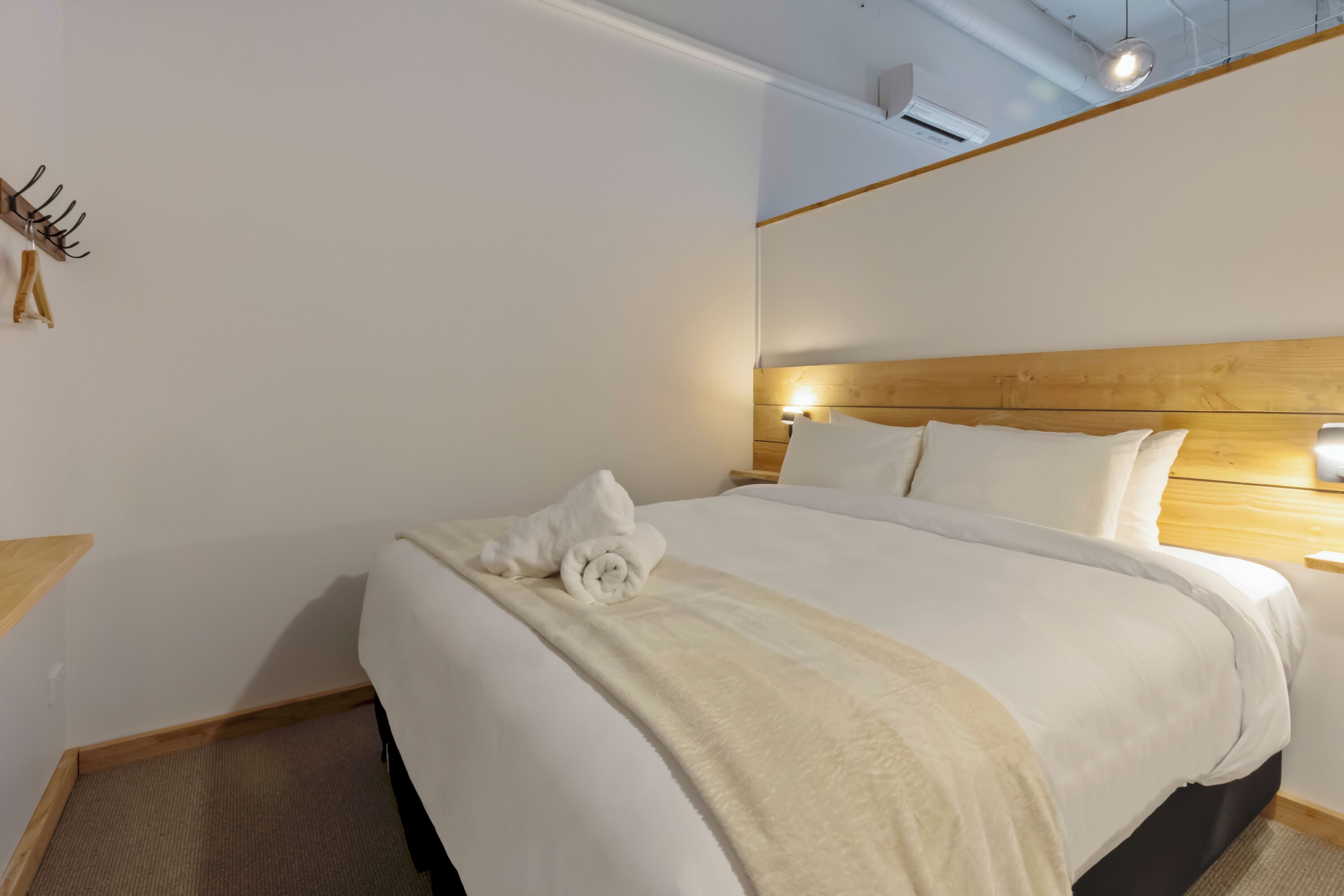 A neatly made bed with white linens and a beige throw blanket, a wooden headboard, and a bedside table with a lamp.