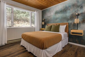 A bedroom with a large bed, wooden headboard, a nightstand, a wall-mounted lamp, and a window with curtains. - Fall Foliage • Views • Hike Appalachian Trail • Ski Hatley & Explore Asheville (Mars Hill)