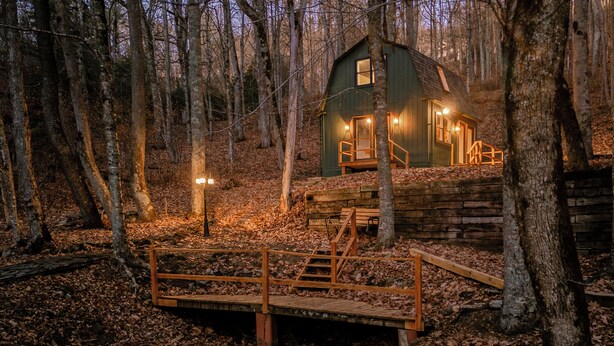Una cabaña rústica con una terraza de madera y escaleras que conducen a la entrada, rodeada por un bosque.