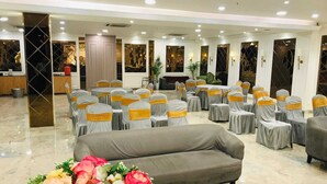 A conference room with rows of chairs covered in grey and yellow sashes, a grey sofa, and a floral arrangement. - Hotel Kingston House Lucknow (Lucknow)