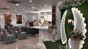 A hotel reception area with a green artificial grass area, a reception desk, and several chairs with grey covers. - Hotel Kingston House Lucknow (Lucknow)