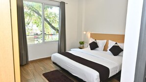 A hotel room with a large bed, a small bedside table with a plant, and a window with curtains. - Hotel Kingston House Lucknow (Lucknow)