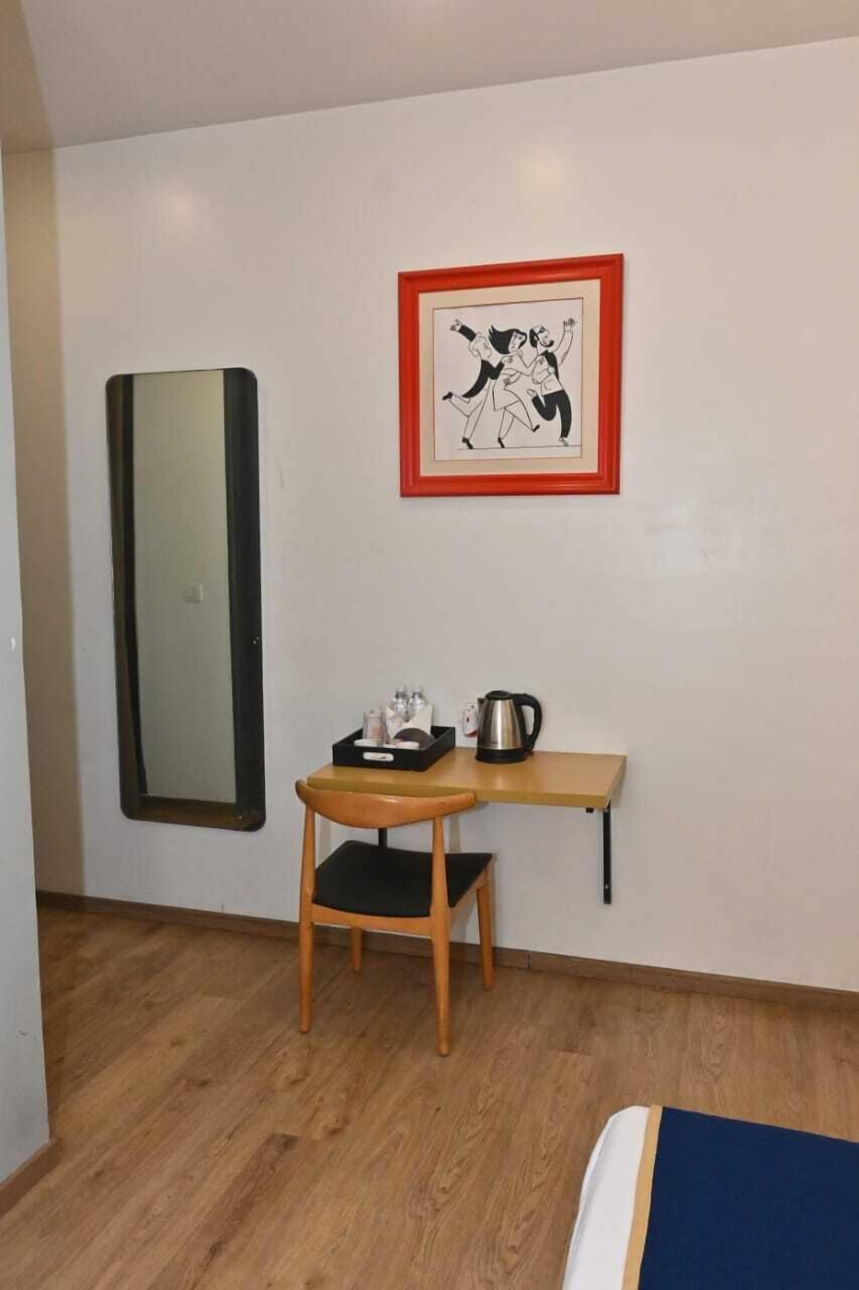 Een kleine kamer met een bed, een bureau met een stoel, een waterkoker en een lijst met een afbeelding aan de muur.