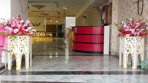A hotel lobby with marble flooring, a reception desk, and decorative floral arrangements. - Hotel The SS Galaxy (Raebareli)