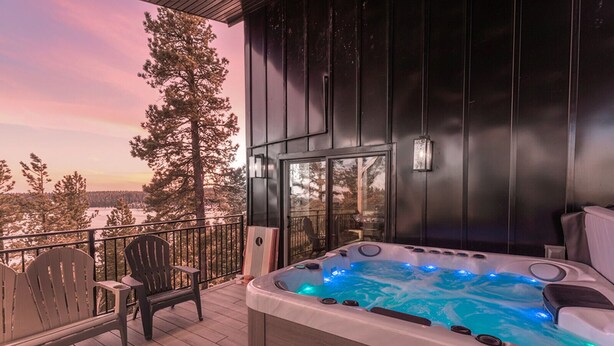 Een hottub op een houten terras met stoelen, met uitzicht op een besneeuwd landschap.
