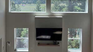 Een kamer met een schuine kap, dakramen, een flatscreen-televisie en een open haard.