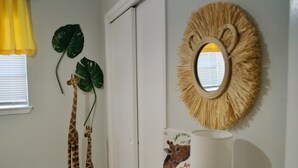 A room with a white door, a mirror with a straw-like frame, a giraffe decoration, and a book titled "An Animal Whispers." - The Elisha House - Cozy Stay Near Local Eats (Katy)