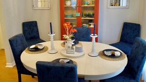 A dining table set for four with blue upholstered chairs, a white tablecloth, and a glass cabinet with dishes behind. - The Elisha House - Cozy Stay Near Local Eats (Katy)