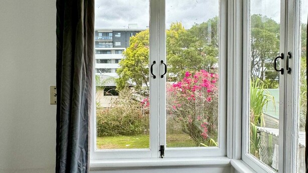 A window with a view of a building and a pink flowering bush. - Affordable Chermside Home near Hospital & Westfield (Chermside)